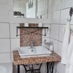 Bathroom with sink on stone top, mirror, and towels on hooks.