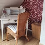 Desk with chair, wallpapered wall, wooden floor, and closet in room.