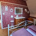 Bedroom with red patterned walls, white bed frame, and wooden dresser.