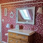 Bedroom with patterned red walls, mirror, and wooden dresser.
