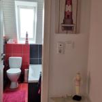 Bathroom with toilet, bathtub, and window. Hallway decorated with wall art and swimmer figurine.