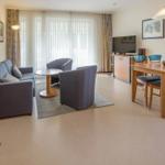 Wohn- und Essbereich mit Sofa, Stühlen und TV. Holztisch mit Stühlen.