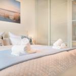 Schlafzimmer mit Bett, Kissen und Handtüchern. Wandbild und Kleiderschrank sichtbar.