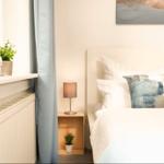 Schlafzimmer mit Bett, Nachttisch, Lampe und Pflanzen an Fensterbank.