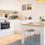 Küche mit Essbereich, weißer Arbeitsfläche und Holztisch mit Stühlen.