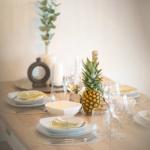 Tisch gedeckt mit Teller, Gläsern und einer Ananas als Zentrum.
