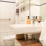 Badezimmer mit Waschbecken, Toilette und Dusche. Weiße Fliesen, Spiegel und Handtuch.