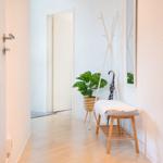 Flur mit Sitzbank, Pflanze und Kleiderständer. Holzboden und weiße Wände.