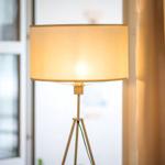 Eine Stehlampe mit einem hellen Schirm steht neben einem Fenster und Vorhängen.