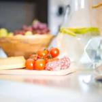 Auf der Arbeitsplatte stehen Käse, Tomaten und Wurst neben einem Wasserglas.