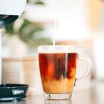 Kaffee wird in ein Glas gegossen, daneben steht eine Kaffeemaschine.