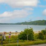 Strand mit Strandkörben und Wald im Hintergrund unter blauem Himmel mit Wolken.