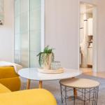 Ein Wohnzimmer mit gelbem Sofa, runden Tischen und einer Pflanze auf dem Tisch.
