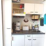 Küche mit weißen Schränken, Spüle, Kaffeemaschine und Mikrowelle.