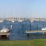 Hafen mit Booten und Stegen, Blick auf Wasser und Segelyachten im Hintergrund.