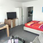 Schlafzimmer mit Bett, Fernseher, Esstisch und Küche im Hintergrund.