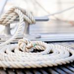 Ein weißes Seil liegt auf einer Holzoberfläche und ist um einen Metallsteg gewickelt.