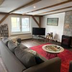 Wohnzimmer mit Sofa, Fernseher und Kamin. Holzbalken und roter Teppich.