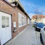 Haus mit weißen Fenstern und Tür, gepflasterte Straße mit geparkten Autos.