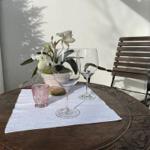 Runder Tisch mit Blumenvase, Gläsern und Stuhl im Freien.