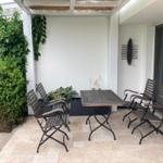 Terrasse mit Tisch und vier Stühlen, umgeben von Pflanzen und einer weißen Wand.