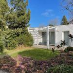 Weiße Villa mit Terrasse und Garten. Blick auf den Rasen und die Bäume.