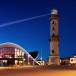 Hafenbeleuchtung und Leuchtturm bei Nacht mit modernem Gebäude im Hintergrund.