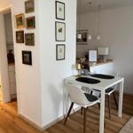 Essbereich mit Tisch und Stühlen, Wand mit Bildern, Holzboden und Küchenbereich im Hintergrund.