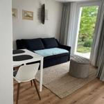 Wohnbereich mit Sofa, Tisch und Stuhl. Durchgang zur Terrasse mit Blick auf Garten.