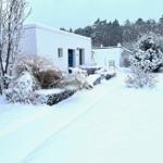 Schnee bedeckt einen weißen Gartenweg vor einem kleinen Haus mit blauer Tür.