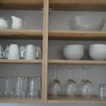 Wooden cabinet with dishes and glasses. White mugs, bowls, and wine glasses are visible.