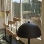 Wooden figures on a black stand sit on a marble countertop next to a window.