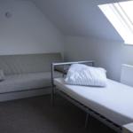 Room with sofa bed and single bed under sloped ceiling with skylight.