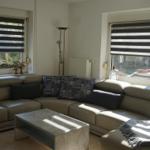 Living room with sectional sofa, coffee table, and windows with blinds.