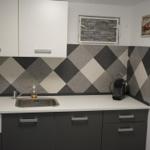 Kitchen with white surfaces, gray cabinets, and black-and-white mosaic on the wall.