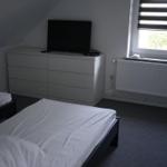 Two beds, dresser with TV, window with blinds, and radiator.