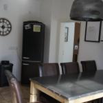 Dining area with table, chairs, and refrigerator. Hanging lamp and wall clock visible.
