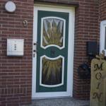 Entrance door with green frame and glass panels. Wooden sign with lettering stands beside it.