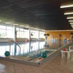 Innenpool mit Liegestühlen, Pflanzen und Spielzeug. Decke mit Holzverkleidung und Fensterfront.