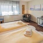 Zimmer mit zwei Betten, Sessel und Wandbildern.