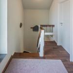 Hausflur mit Holzfußboden, Treppe und Fenster. Wanddekoration und Tür sichtbar.