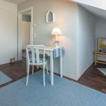 Zimmer mit Schreibtisch, Stuhl, Fernseher und Holzboden.