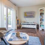 Wohnzimmer mit Sofa, Sessel, Tisch und Fernseher. Fenster mit Blick auf Terrasse.