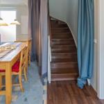 Essbereich mit Tisch, Stühlen und Tischdecke. Treppenhaus mit Holztreppe und Vorhängen.