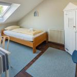 Zimmer mit Dachfenster, Bett, Schrank und Tisch mit Stühlen.