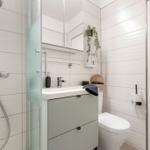 Badezimmer mit Dusche, Waschbecken und Toilette. Weiße Fliesen und graue Schrank.