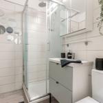 Badezimmer mit Dusche, Waschbecken und Toilette. Wand mit runden Spiegeln und Pflanze.