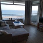 Wohnzimmer mit Sofa, Couchtisch und TV. Große Fenster und Balkontür mit Meerblick.