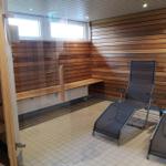 Sauna mit Holzwand, Liegen und Fenster. Tür führt in einen separaten Raum.