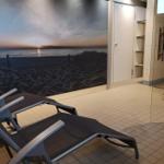 Liegende Stühle vor Strandbildwand, Sauna und Dusche im Hintergrund.